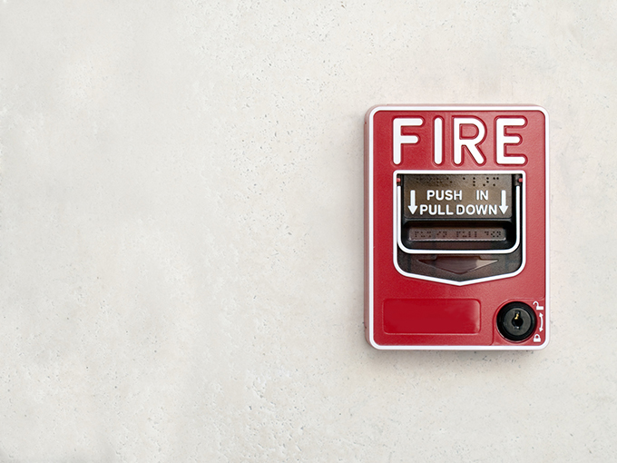 Image of white wall with red fire alarm to depict the important of fire safety procedures for WellBiz franchisees.